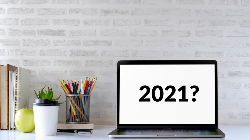 A computer sitting on top of a well oraganized desk. The computer screen displays the words "2021?"